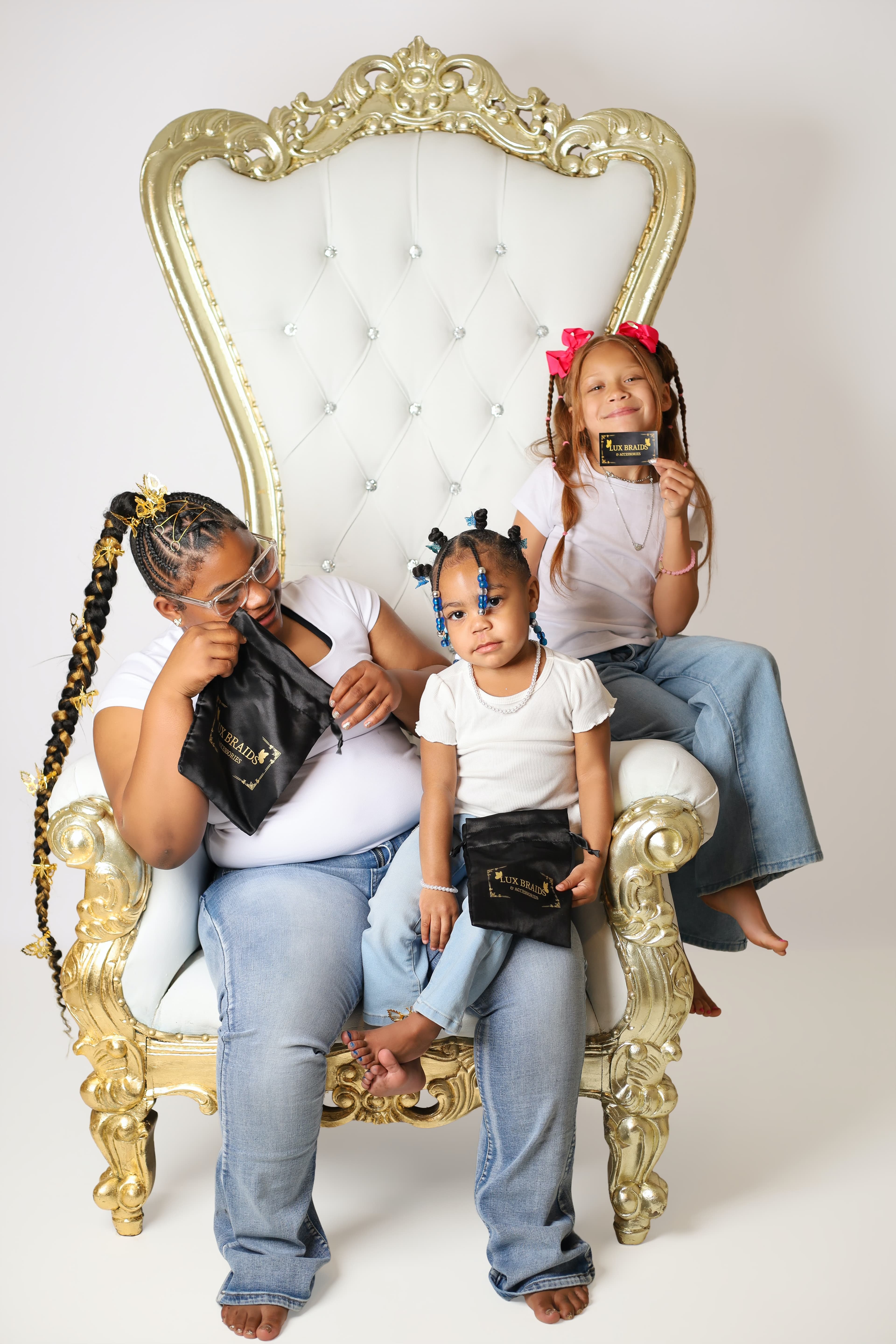 Woman and two children on a white and gold throne holding branded hair accessory bags.