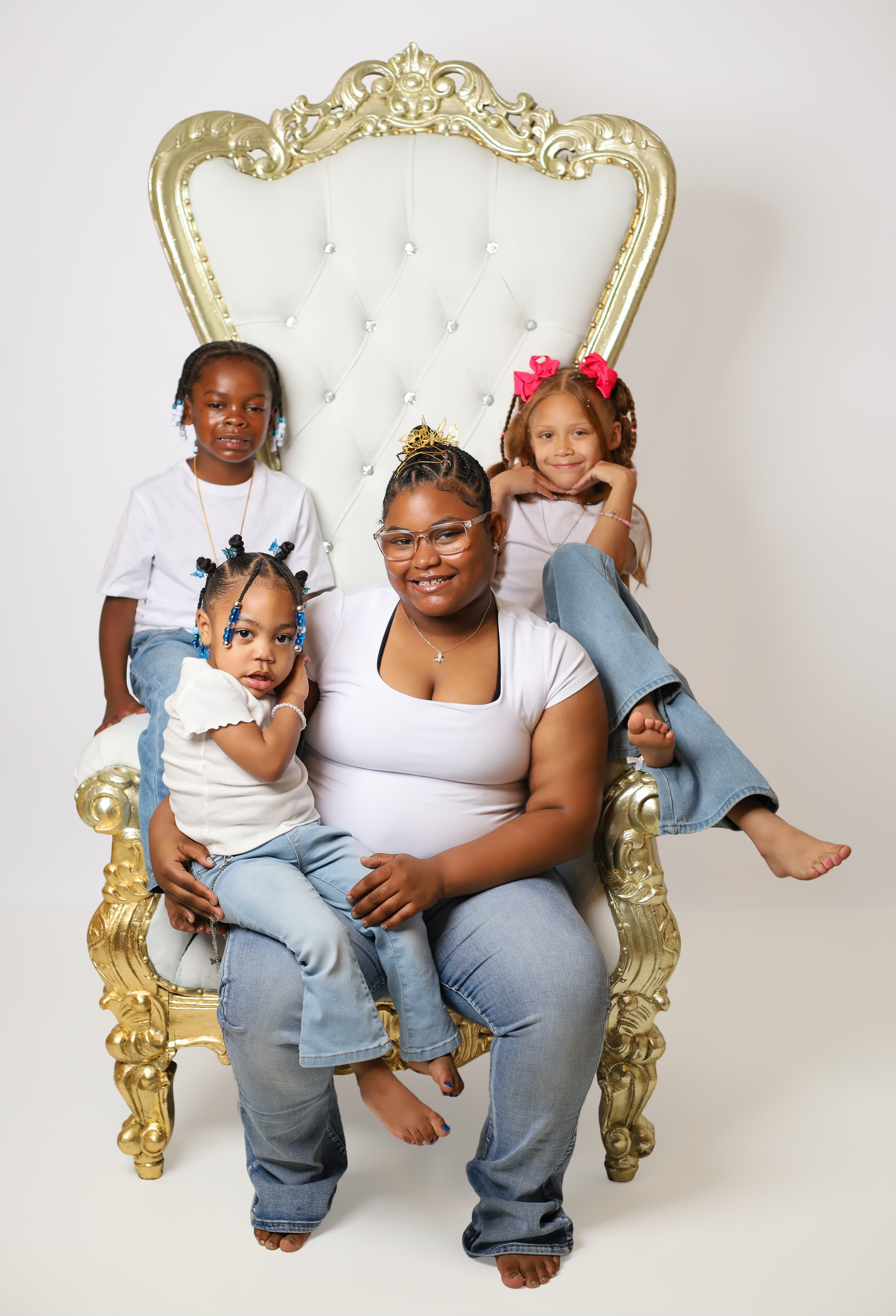 Woman and three children in white shirts and jeans pose on a gold throne.