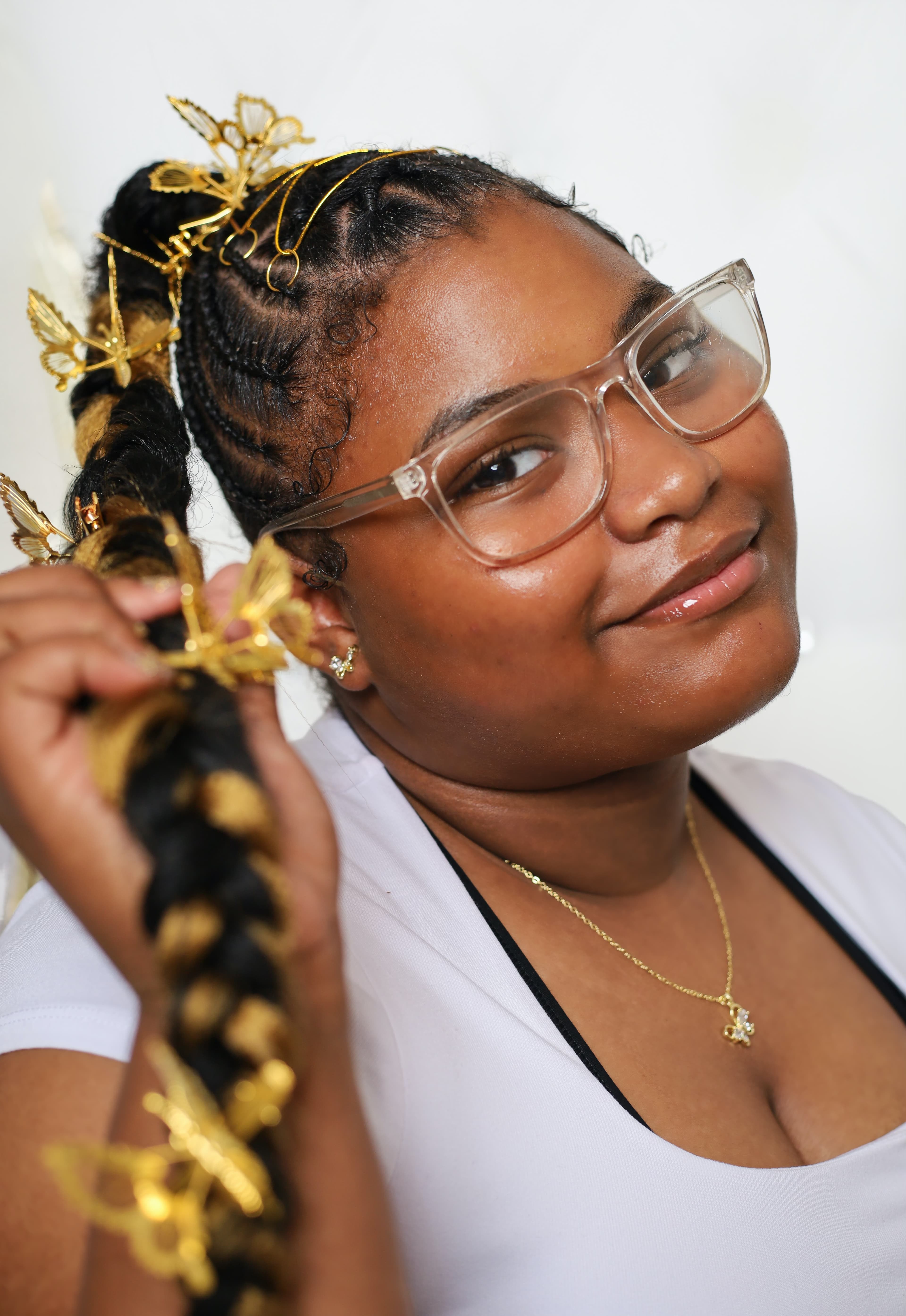 Smiling woman with glasses holding her braided ponytail adorned with gold butterfly hair accessories.